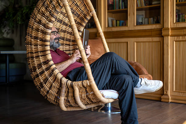 Bearded man sitting on wicker swing manages his business with computer.
