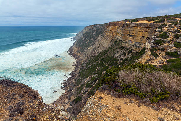 istock A dramatic coastal cliff overlooks turquoise waves crashing onto a secluded sandy beach, framed by rugged rock formations and wild vegetation 2234128764
