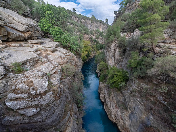Steep rocky cliffs and a turquoise river in Koprulu Canyon, Antalya. The canyon edges are covered with green trees.