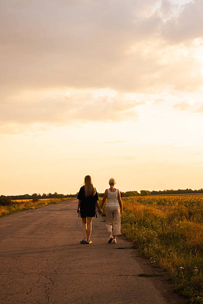 istock Two women walking hand in hand along a rural road at sunset surrounded by fields 2234132824