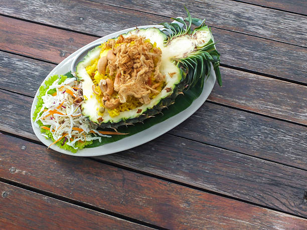 Thai-style pineapple fried rice served in a pineapple on a wooden table.