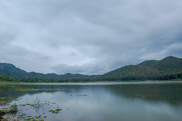 A wide view of the lake under an open sky at Huai Lan Reservoir, Thailand. The expansive water surface mirrors the blue sky, creating a calm and serene atmosphere surrounded by natural beauty. This peaceful scene captures the harmony between land, water, and sky, making it a perfect representation of rural Thailand’s tranquil landscapes.