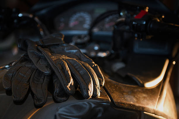 Black motorcycle gloves placed on a bike's dashboard, illuminated by soft light in a dimly lit area at dusk