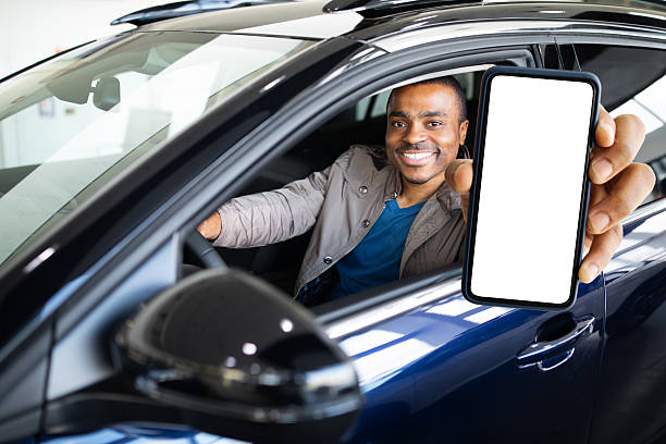 istock Smiling black man sitting in driver seat holding smartphone with blank screen 2234176774