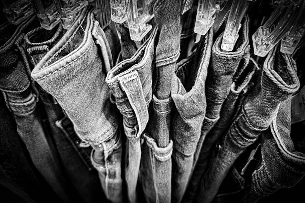 Looking down at several pairs of jeans on wardrobe hangers. Monochrome retro fashion background.