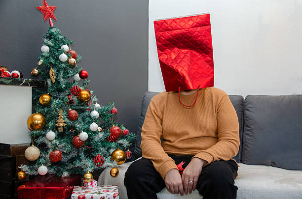 Man wearing a gift bag in his head with a Christmas tree next to it