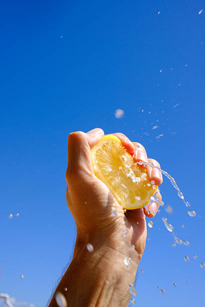 Hand squeezing fresh lemon juice against blue sky