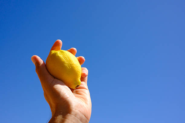 Holding a bright yellow lemon against a vibrant blue sky, creating a striking contrast that evokes a refreshing feeling of summer and the essence of natural, healthy living
