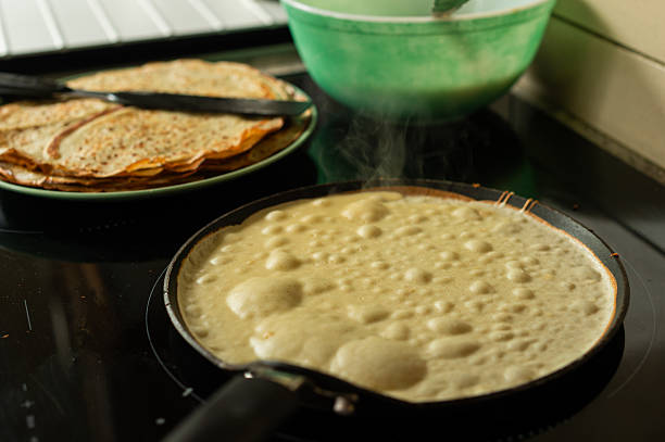 A pancake fries on a skillet, with a plate of ready pancakes and batter behind, perfect for cooking vibes. Ideal for food visuals, home recipes, or cozy lifestyle content with a warm appeal.