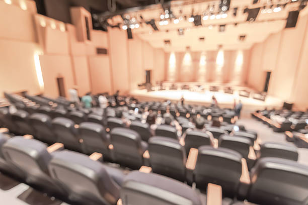 Auditorium blur background with amphitheater stage show, crowd audience seat rows in blurry theatre hall backdrop for seminar conference meeting, performing arts, concert event, music performance