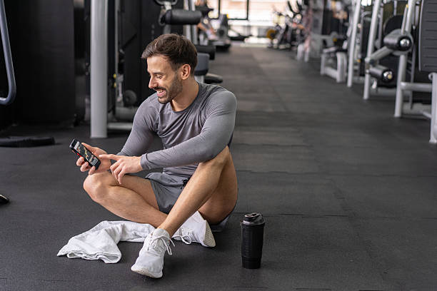 istock Man at gym checking phone while sitting on the floor 2234210496