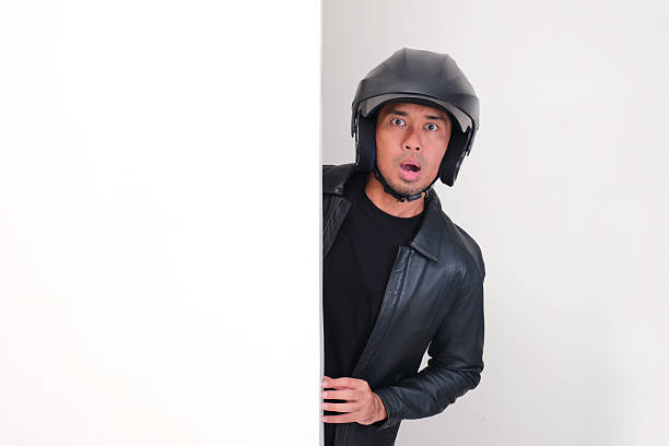 Motorcycle rider wearing helmet peeking behind wall with shocked face expression