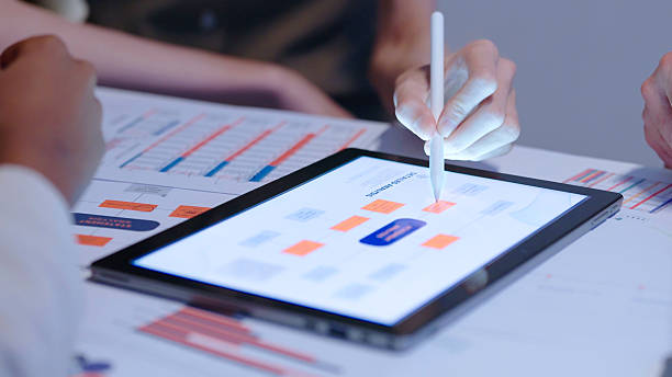 Close up Diverse Collaborative Business people meeting with Digital Devices computer brainstorming the financial report paperwork document analyzing data  planning strategies displays a graph  chart in a modern business technology overworked late at night