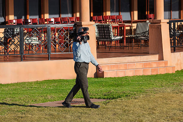 arab man cameraman with a camcorder on the shoulder filming outdoors , professional digital camera, outdoors event on the grass