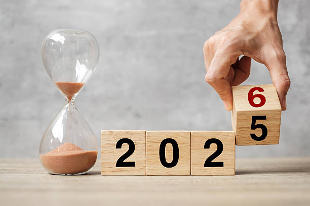 istock hand flipping block 2025 to 2026 text with hourglass on table. Resolution, time, plan, goal, motivation, reboot, countdown  and New Year holiday concepts 2234230193