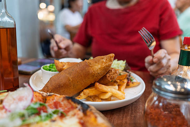 Close-up of crispy battered fish served with golden fries, mushy peas, and tartar sauce on a white plate in a restaurant setting.