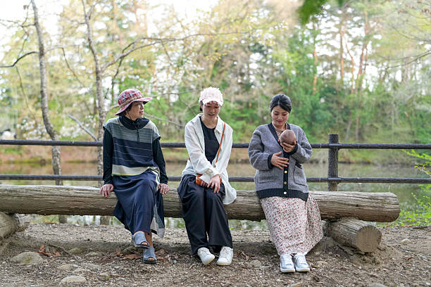 Three women sitting on a log in a park. One of them is holding a baby. Scene is peaceful and relaxing