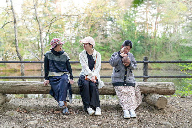 Three women sitting on a log in a park. One of them is holding a baby. Scene is peaceful and relaxing