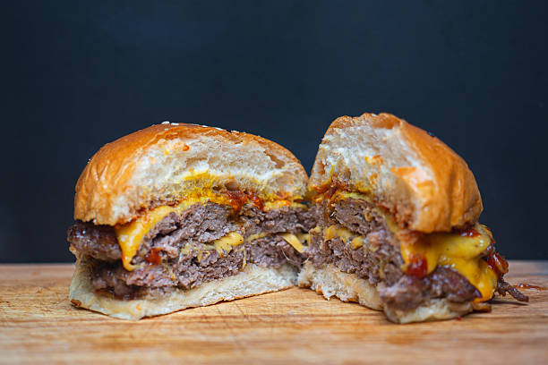 Juicy double cheeseburger cut in half on wooden board with melted cheddar and grilled beef