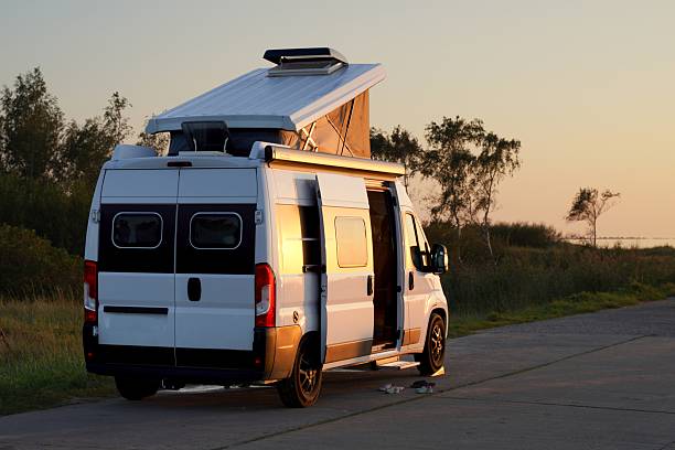Modern camper van parked outdoors at sunset with open roof and doors, symbolizing freedom, adventure and van life. Concept of travel, camping and outdoor lifestyle.