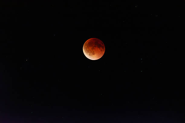 Beautiful capture of a red lunar eclipse with the glowing moon surrounded by stars in the dark night sky. Blood moon