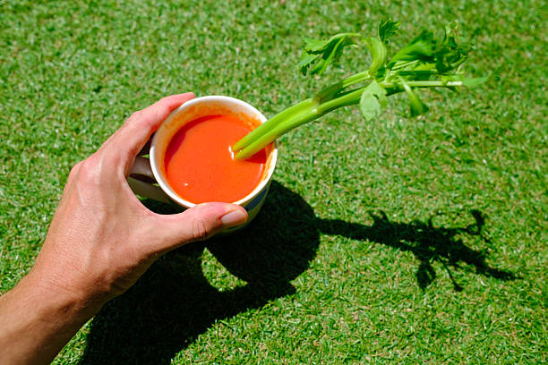 Hand holding a mug of refreshing spanish gazpacho, also called andalusian gazpacho, a cold tomato-based raw vegetable soup, over green grass on a sunny day