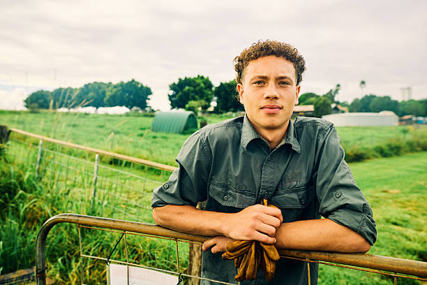 Portrait of a young farmer leaning on a gate in a lush green field, representing sustainable agriculture and environmental conservation