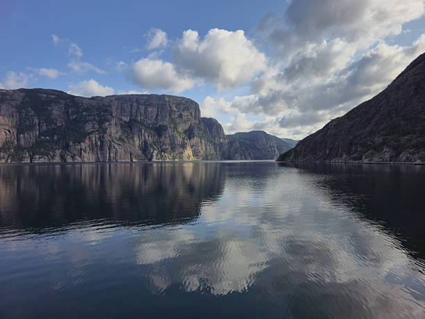 Breathtaking view of Lysefjord, showcasing towering cliffs mirrored in the calm waters. Clouds drift lazily overhead, creating a serene and picturesque atmosphere in this stunning Norwegian landscape.