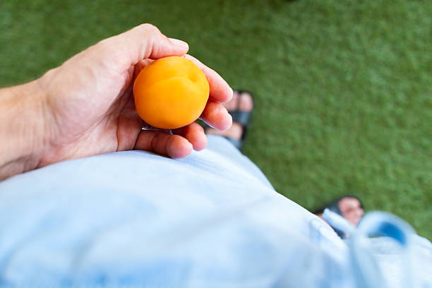 Hand holding a ripe apricot, showcasing its vibrant color and soft texture against a blurred green grass background, highlighting the fresh, juicy fruit ready for enjoyment