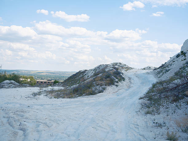 Winding path leads through desolate chalk quarry landscape. White terrikons and low-lying vegetation under cloudy sky create a unique artificial scenery in Sloviansk, Ukraine.