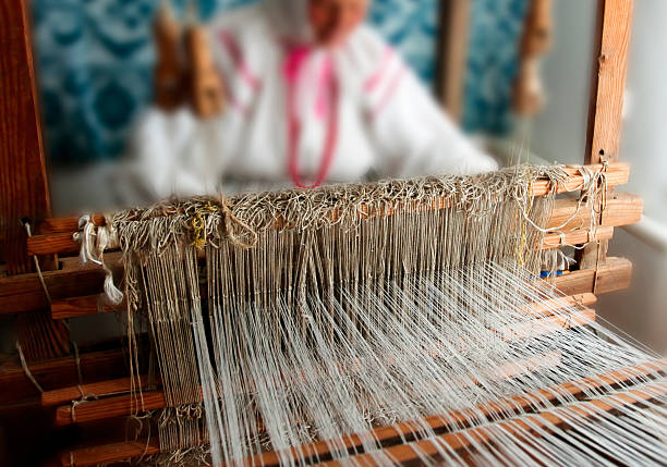 A skilled artisan works diligently at a wooden loom, weaving fine threads into intricate patterns within a sunlit space.