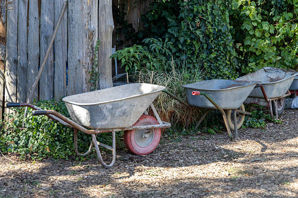 Old rusty red wheelbarrow beside a wall on a sunny day.