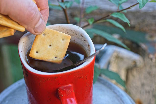 istock fingers hold one brown square cracker cookie dipped in black coffee 2234270751