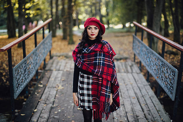 istock Chic Woman in Red Beret and Plaid Wrap Standing on Rustic Bridge in Autumn Forest Setting 2234276996