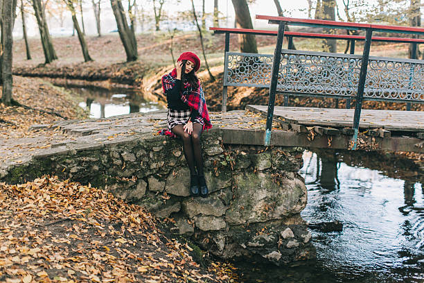 Young Woman Sitting on Rustic Stone Bridge in Autumn Forest