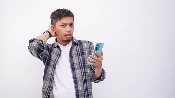 istock Asian man looking up while holding mobile phone and showing confused face expression on white background 2234280313