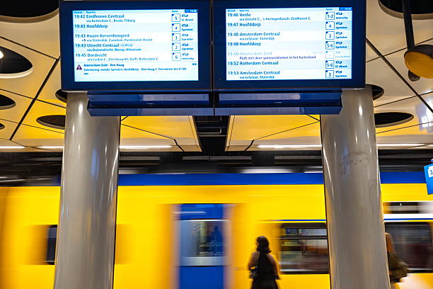 Amsterdam Schiphol Airport, Holland, August 25, 2025. Train schedule or info board and blurred, moving, yellow train carts in the background inside underground station