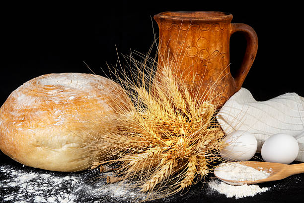 Traditional baking ingredients arranged with rustic pottery and wheat at a kitchen table