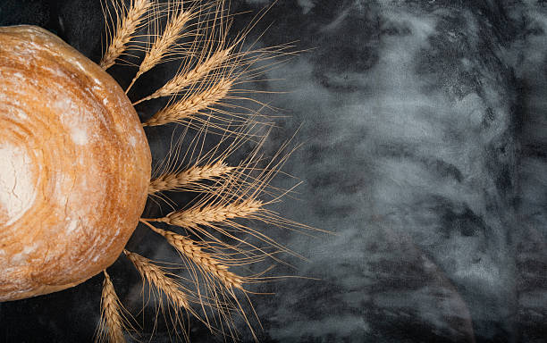 Rustic Bread Loaf with Wheat Stalks on a Dark Flour-Dusted Surface