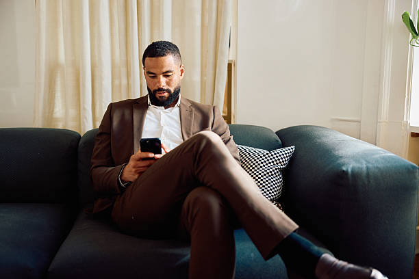 istock Focused business man using a smartphone while sitting cross legged on a sofa in an office lounge 2234284457