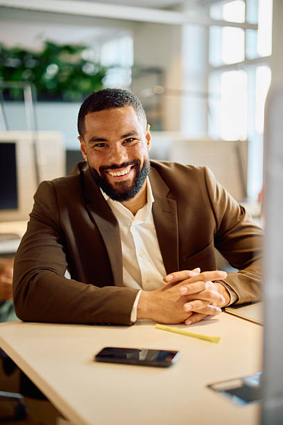istock Portrait of a smiling professional man looking at camera while sitting at a desk with hands clasped in a modern office 2234284505