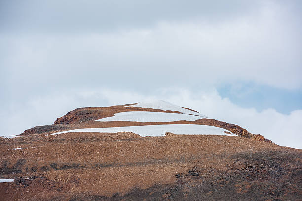 istock Sunlit snowy pointy peak under gray cloudy sky. Triangle shaped snow mountain top in bright sun. Stony hill of pyramid shape in changeable weather. Sharp rocky snowbound pinnacle in overcast sunny day 2234288503