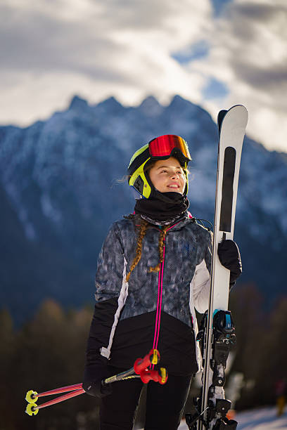 Young skier girl holding skis and looking at mountain peaks