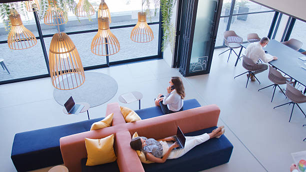 istock Overhead View Of Modern Open Plan Office With Staff Working Around Table And Breakout Seating Area 2234289534
