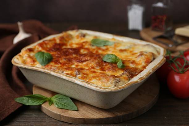 istock Delicious cooked lasagna in baking dish and basil on wooden table, closeup 2234290981