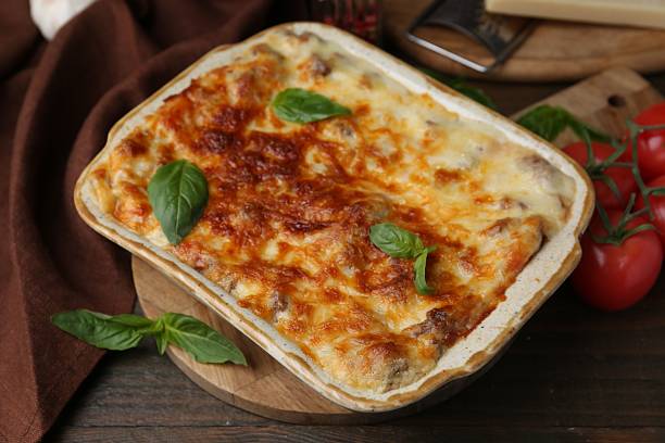 istock Delicious cooked lasagna in baking dish, basil and tomatoes on wooden table, closeup 2234291132