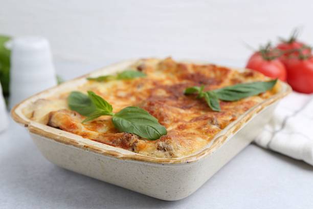 istock Delicious cooked lasagna in baking dish and basil on light grey table, closeup 2234291148