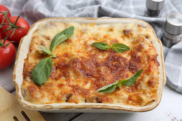 istock Delicious cooked lasagna in baking dish and basil on table, closeup 2234291274