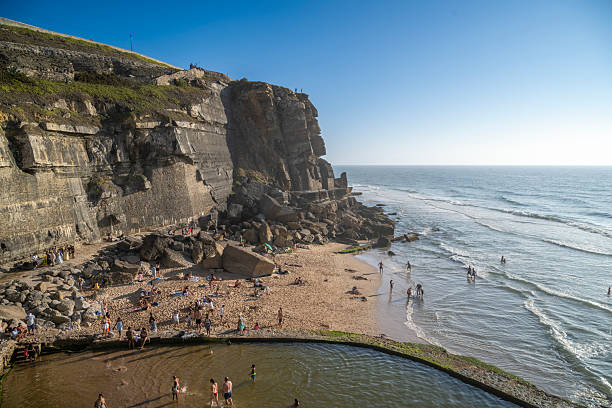 19 August 2025 Azenhas do Mar, Portugal. Tourists enjoy the sandy beach and natural pool at Azenhas do Mar, Portugal, beneath dramatic seaside cliffs overlooking the Atlantic Ocean on a sunny summer day.