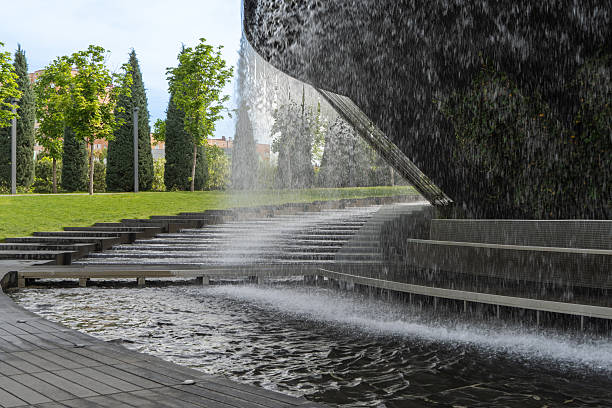 Waterfall flows in streams into granite bed of artificial river. “Infinity” fountain in form of huge bowl is located in public park “Krasnodar” or “Galician Park”.